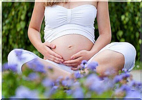 Pregnant woman sitting outside and feeling her stomach.