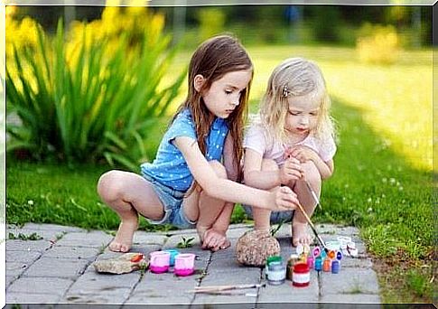 Two girls paint on stones.
