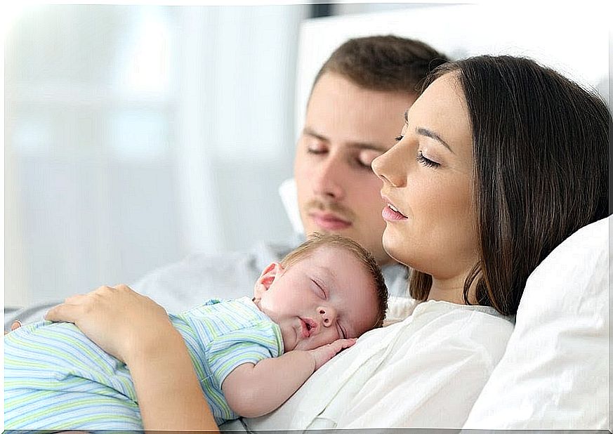 Man and woman sleeping in bed, woman has a sleeping baby on her stomach