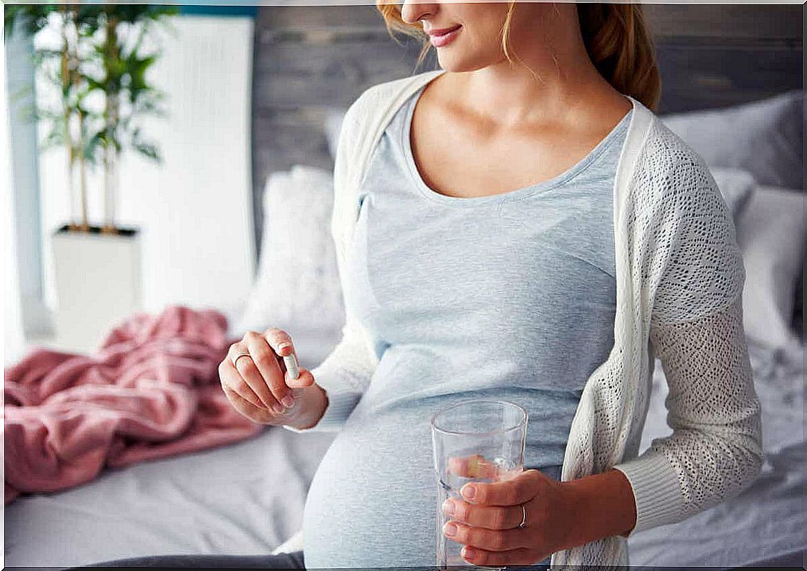 A pregnant woman taking a pill with a glass of water.