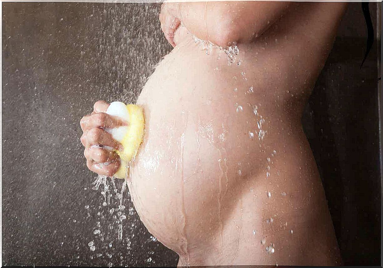 A pregnant woman washing her belly in the shower.