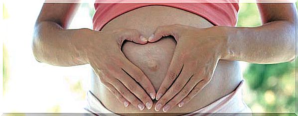 Pregnant woman holding her hands on her stomach in the shape of a heart.