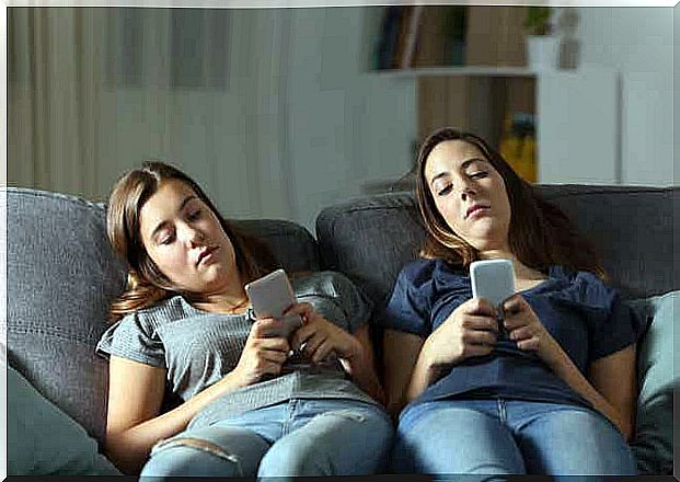 Two young people are sitting on the sofa with their mobile phones in their hands.